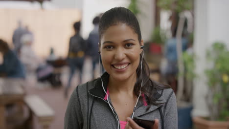 portrait of young mixed race woman smiling cheerful enjoying listening to music wearing earphones using smartphone mobile technology looking at camera