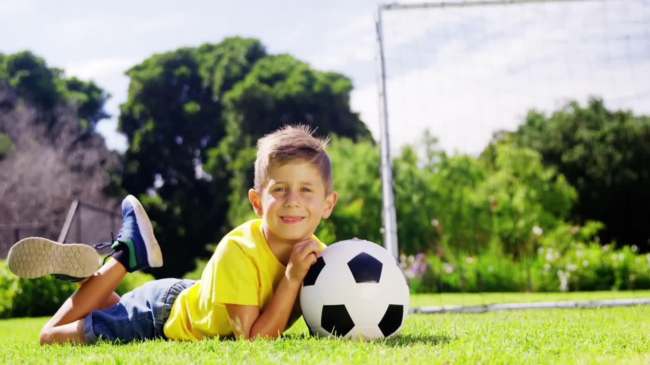 Retrato de menino feliz com bola de futebol deitado no parque