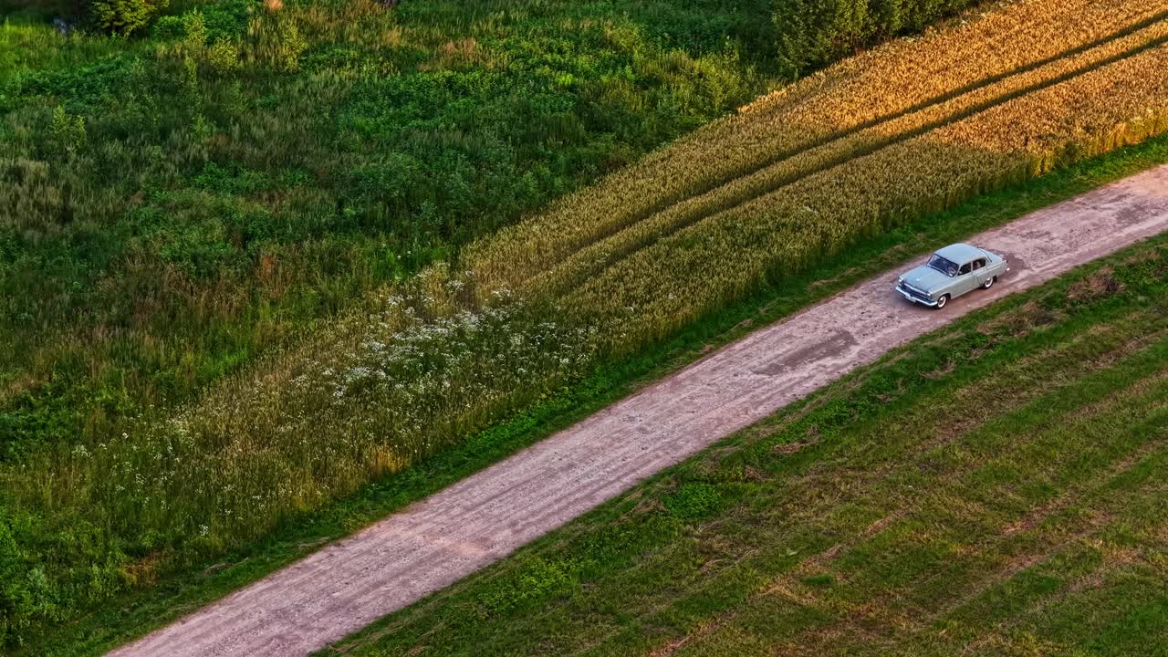 Classic car moves gently along rural path, bathed in warm golden sunlight