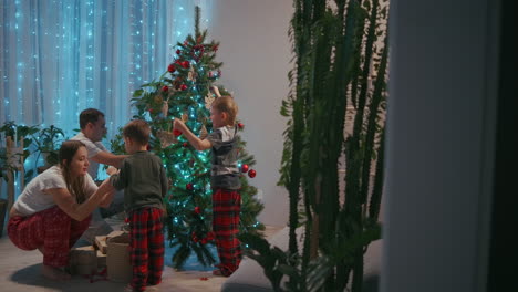 Familia-Feliz-Preparándose-Para-El-Concepto-De-Celebración-De-Las-Vacaciones-De-Invierno-De-Año-Nuevo.-Una-Pareja-Joven-De-30-Años,-Sus-Adorables-Dos-Hijos-Preescolares-Decorando-El-árbol-De-Navidad-Crean-Un-Ambiente-Festivo-En-Una-Casa-Moderna-Y-Acogedora.-Imágenes-4k-De-Alta-Calidad