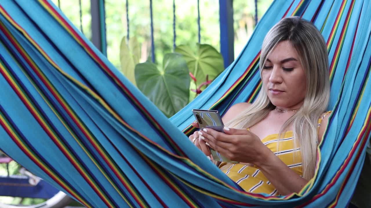 mujer navegando por el teléfono inteligente y descansando en la hamaca