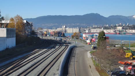 railway tracks leading into an industrial port in vancouver, clear blue sky, mountains in the background, daytime