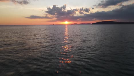la luz del sol naranja se refleja en el agua que ondea tranquilamente en krabi cuando el sol acaba de ponerse debajo de las nubes y está a punto de ponerse
