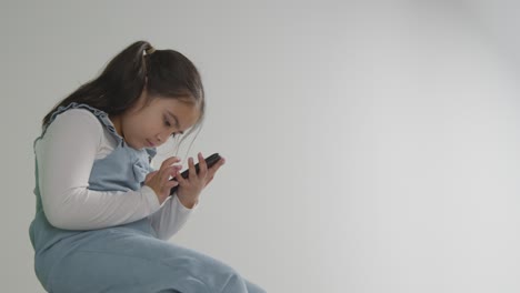 Studio-Shot-Of-Young-Girl-On-ASD-Spectrum-Gaming-On-Mobile-Phone-Against-White-Background