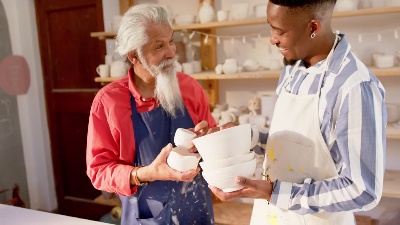 Felici vasai di diverse etnie che tengono ciotole e discutono in uno studio di ceramica, al rallentatore