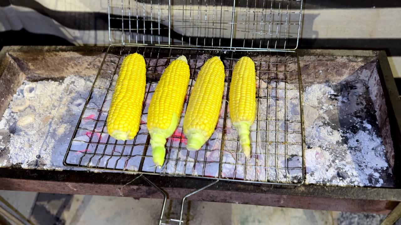 4K close up of four golden corn cobs grilling above glowing charcoal with ash and metal grate texture, creating a rustic outdoor heat-focused cooking scene