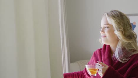 happy caucasian plus size woman uncovering windows with curtain and drinking tea in slow motion