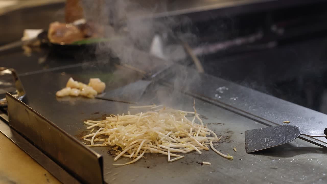 Chef cucina noodles e carne su una griglia calda.