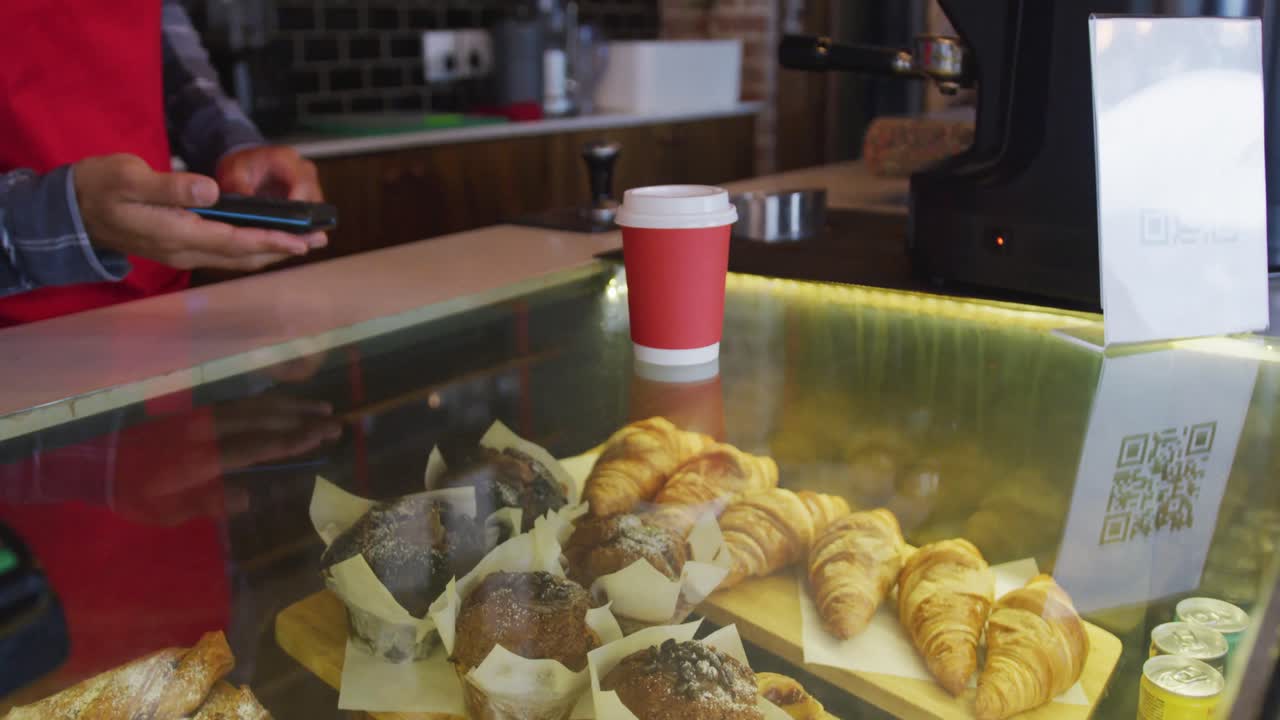 barista de raza mixta que recibe el pago sin contacto del teléfono inteligente por el café para llevar