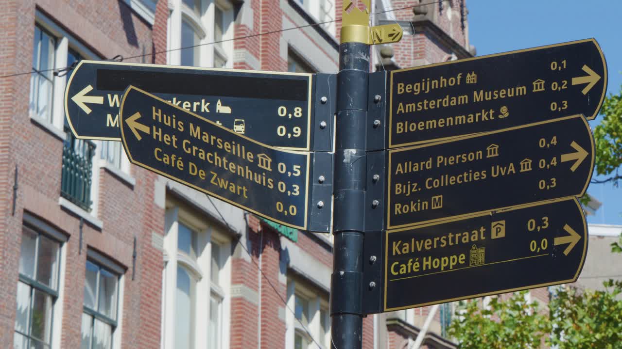 Directional street signs in Amsterdam with historic brick buildings, clear daylight, and slight camera movement