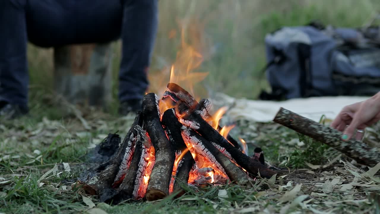 En campist sidder omkring et bål i naturen med brændende træ i flammerne