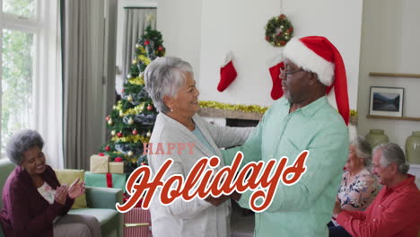 animation of happy holidays text in red over happy diverse senior couple dancing at christmas party