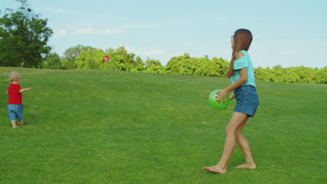 girl playing with ball in green meadow. toddler walking on grass in field