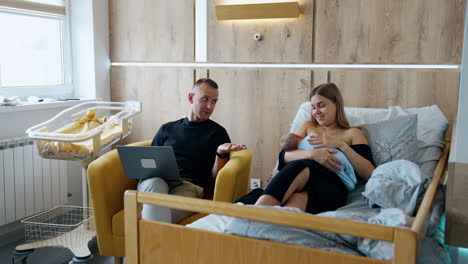 New-made parents having a little argument. Man with laptop in hands speaking to a wife breastfeeding a newborn.