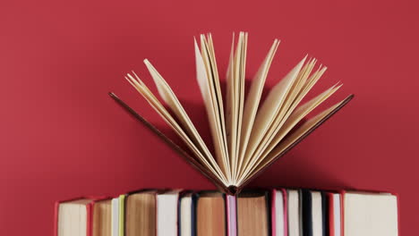 un libro abierto descansa encima de una pila contra un fondo rojo, con espacio de copia