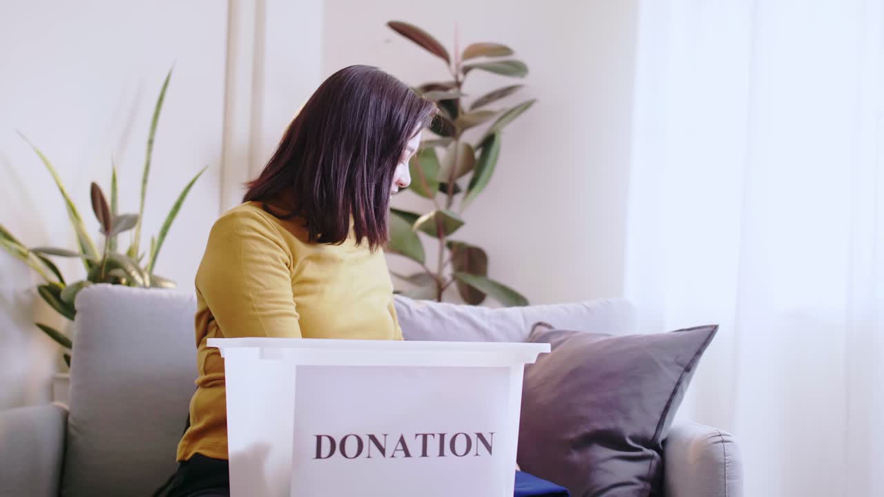mujer asiática seleccionando ropa para donar y poniendo en caja