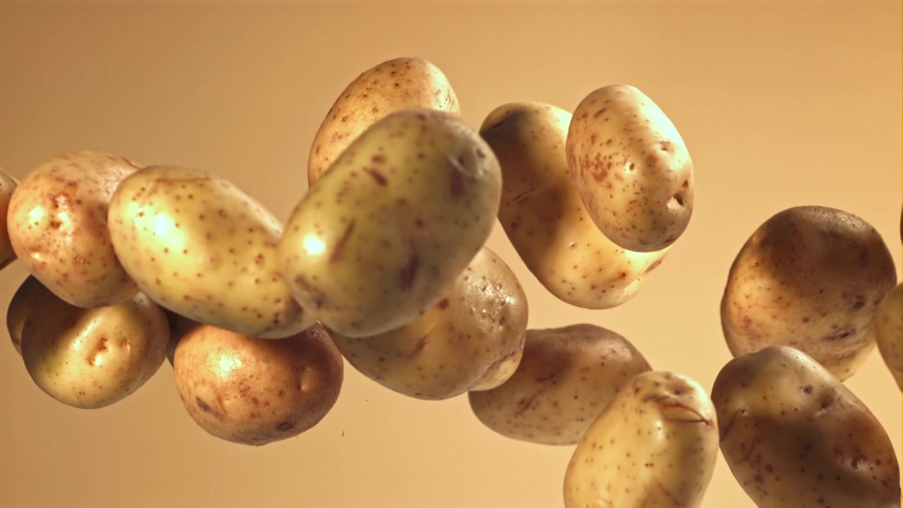 Patate fresche e crude che galleggiano al rallentatore su uno sfondo beige