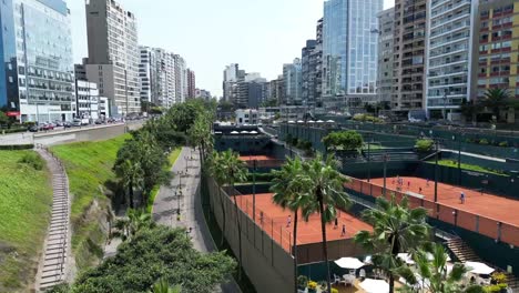 impresionante club de tenis descubierto por un dron aéreo que viaja hacia atrás disparado en medio de edificios, palmeras, árboles, calles históricas y jardines