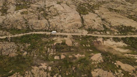 Toma-Aérea-De-Una-Furgoneta-Blanca-Conduciendo-Por-Un-Camino-Rural-Entre-Las-Montañas-De-Argentina