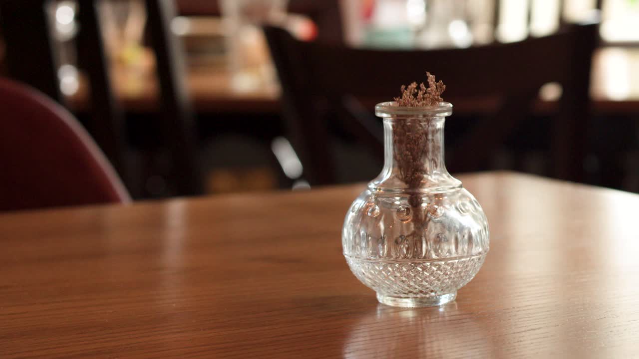 Camera slowly pans across wooden restaurant table with glass vase, soft natural lighting, shallow focus