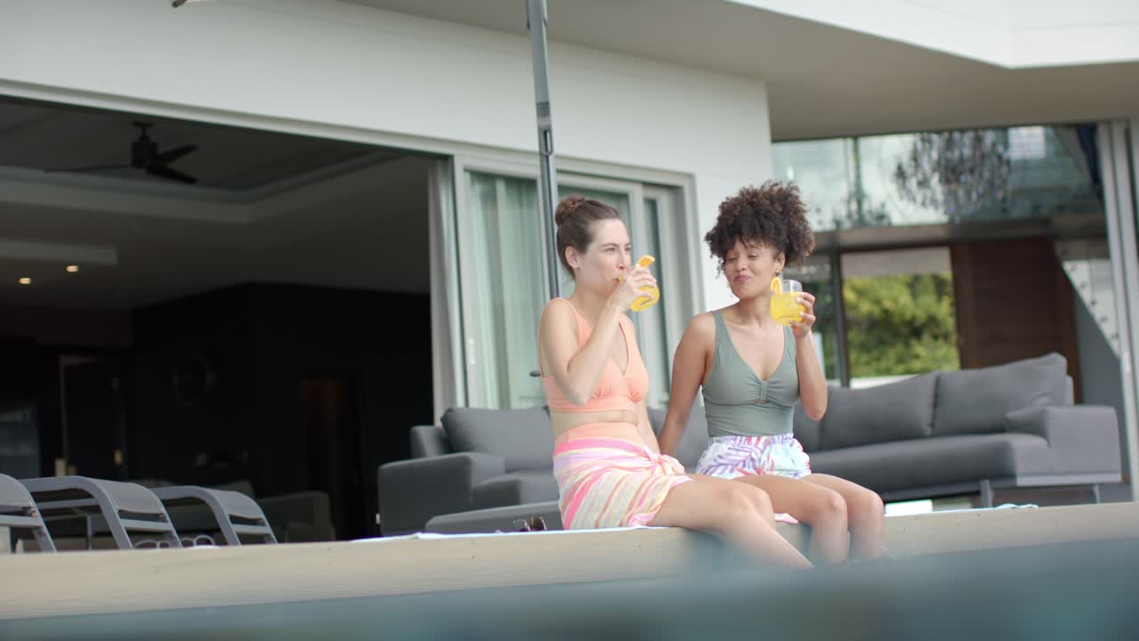 Diverse amiche in bikini che sorseggiano da bicchieri gialli, poi si scambiano sorrisi e si rilassano a bordo piscina.