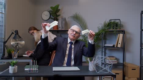 Elderly-man-boss-celebrating-business-success-dancing-with-money-dollar-cash-in-modern-office-room