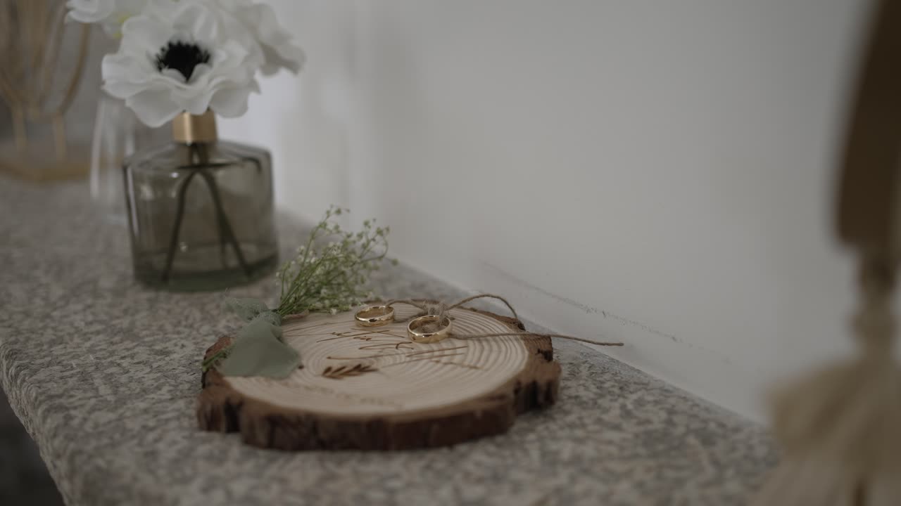 свадебные кольца, лежащие на деревянной платформе, окруженной нежной зеленью