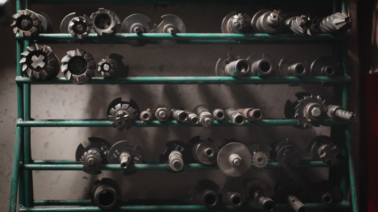 A collection of various industrial metal milling cutters and machining tools neatly organized on a green metal rack