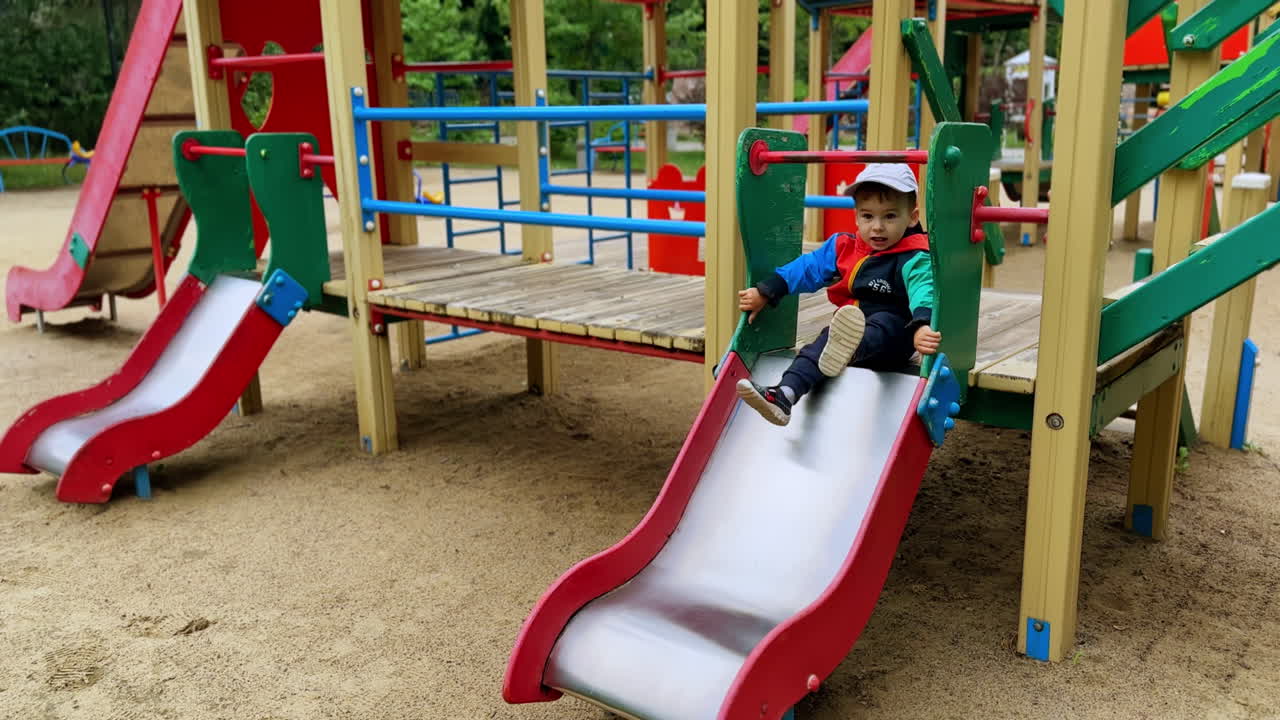 Active baby boy spending time on the playground. Active kid taps his feet energetically and slides down.