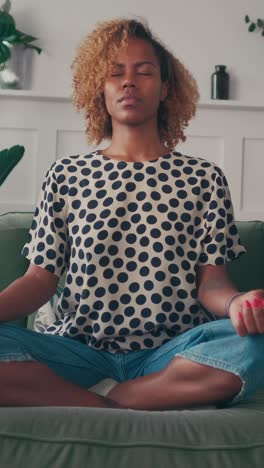 young beautiful african american woman meditates sits on sofa in lotus position
