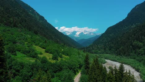 flying over the asphalt road by the mountains with the lush green forest on a sunny day in racha, georgia