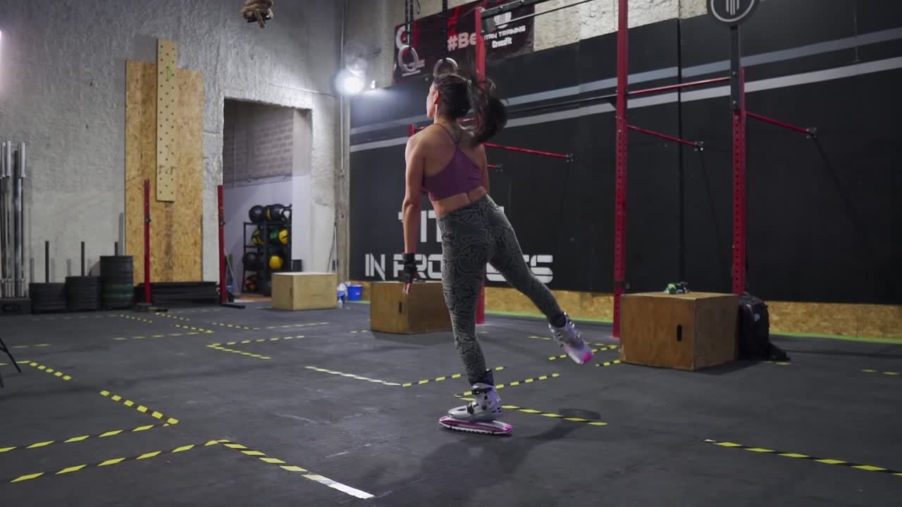 Slow-motion static, shallow focus, one light long back shot of a pretty fit Hispanic model jumping work out wearing fitness clothes