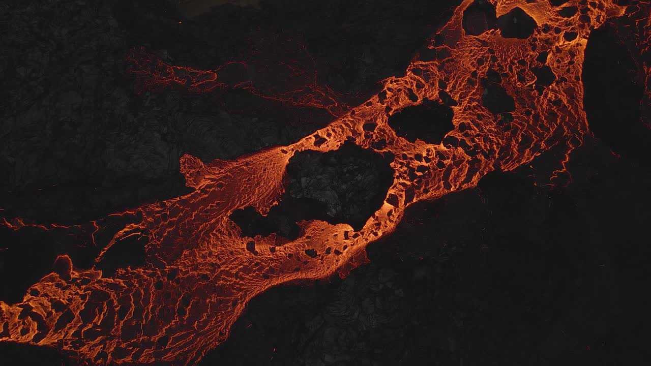 River of glowing lava flows between volcanic rocks