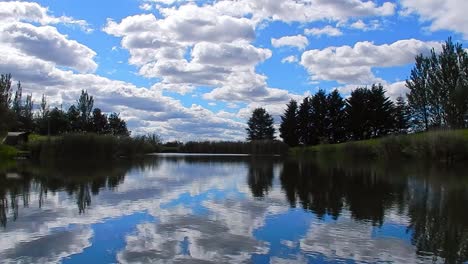 vibrant blue lake water mirror reflection of bright clouds and trees in blue sky