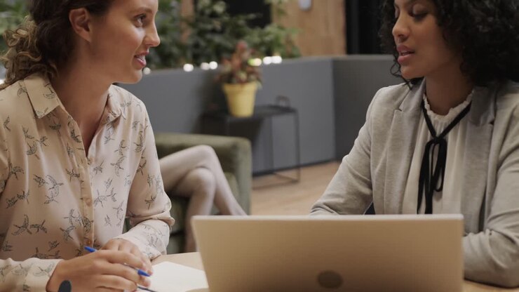 Diverse colleghe in discussione che usano il laptop nella sala lounge dell'ufficio, slow motion
