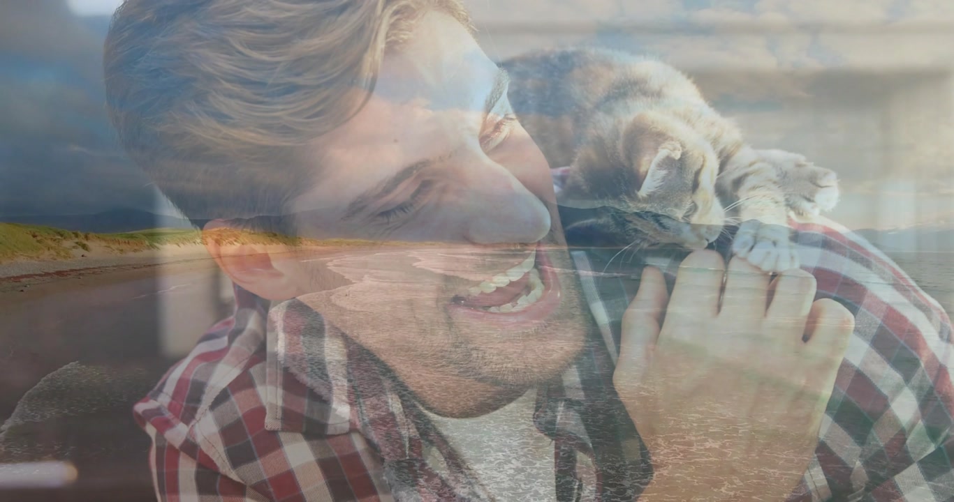 Man wearing plaid shirt holding small tabby kitten on right shoulder at home with beach overlay