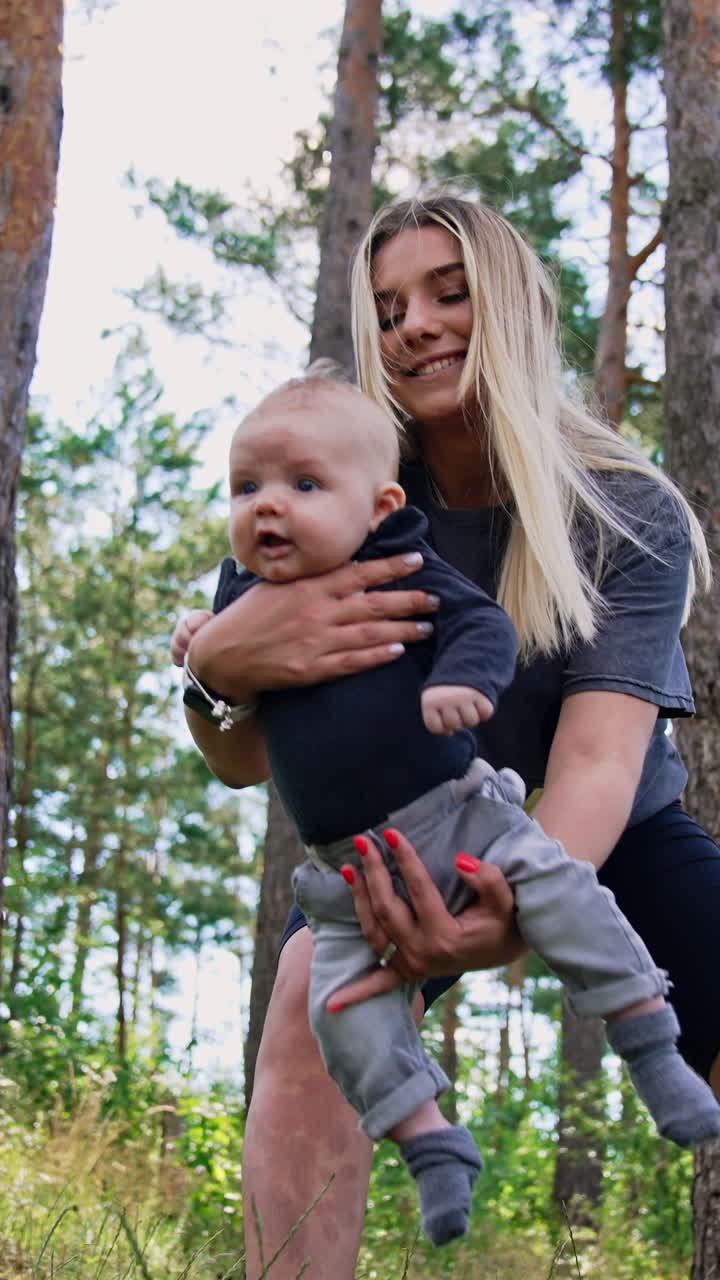 Happy smiling woman waving her cute baby boy. Mom entertaining her child in the nature. Vertical screen. Vertical video