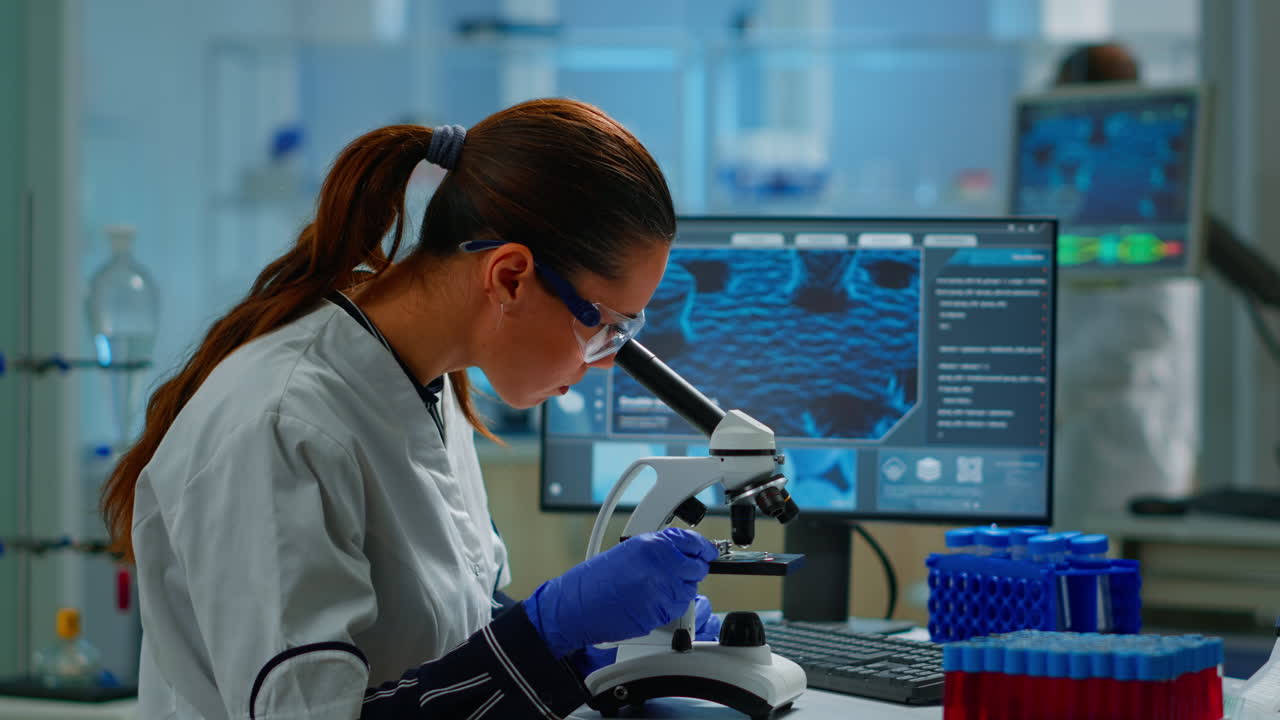 científico que observa muestras biológicas bajo el microscopio escribiendo en la computadora