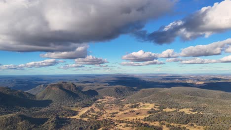 drone captures sweeping panoramic view of rugged bushland, gum trees, and dramatic clouds over warrumbungle national park in afternoon sunlight, with smooth lateral camera movement