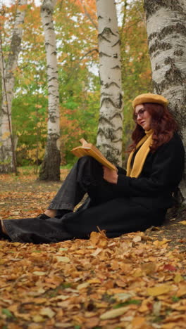 dama en la soledad se apoya contra el árbol, leyendo un libro pensativo en el pacífico parque de otoño, rodeada de hojas doradas caídas, disfruta de la tranquilidad de la naturaleza, perdida en profunda contemplación