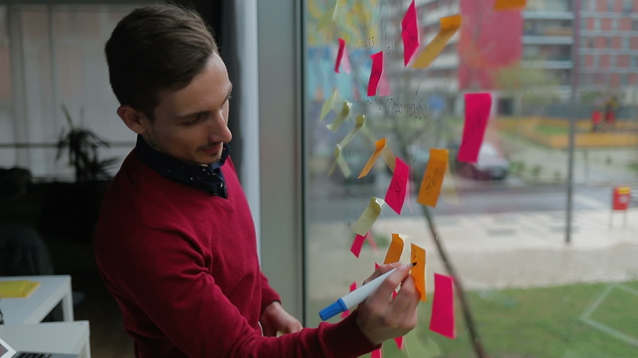 un joven guapo sonriente escribiendo en notas adhesivas en la ventana.