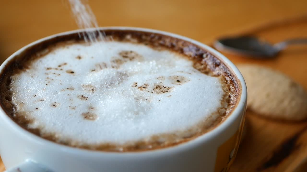 Closeup of a cup of coffee with sugar being added
