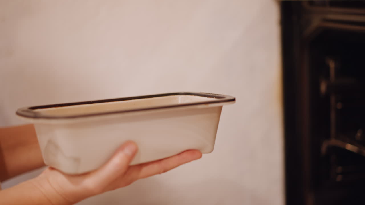 Avó caucasiana colocando suavemente torta de abóbora, guiando a assadeira retangular para a grelha do forno, mangas de renda branca visíveis, massa dourada reluzindo, luz quente da cozinha, preparação festiva carinhosa.