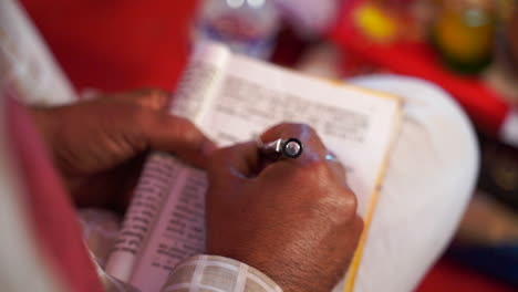 closeup hands of an asian indian male writing with pen on a book printed in foreign language