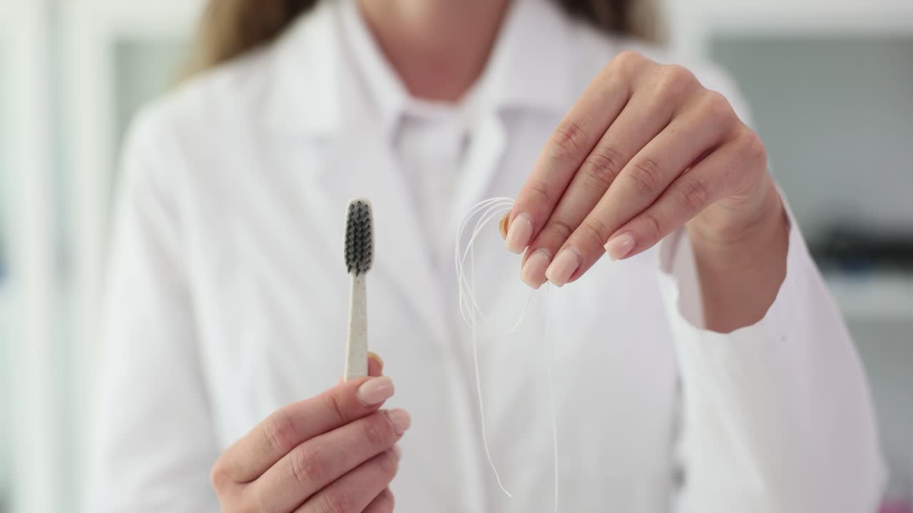 A person in a white coat holding a toothbrush and dental floss for oral hygiene