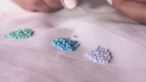 closeup of woman´s hands threading a bead on a needle