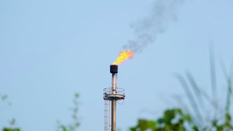 Petroleum-refinery-gas-flare-blazing-fire-pouring-thick-black-smoke-into-the-blue-sky-from-chimney-stack---4K-footage