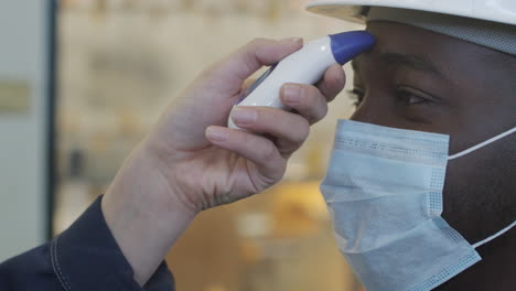 taking temperature of plant worker in face mask