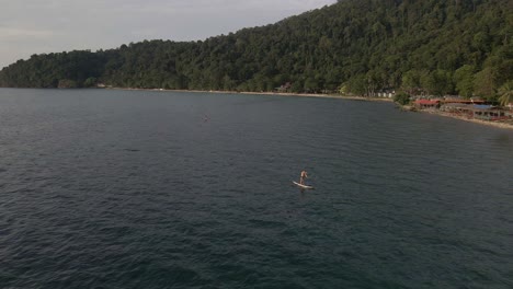 Vogelperspektive-Aus-Der-Vogelperspektive,-Die-Sich-Schnell-Rückwärts-Bewegt,-Aufsteigender-Dolly-Aufnahme-Eines-Mannes,-Der-Auf-Einem-Sup-Paddle-Board-In-Türkisfarbenen,-Tropischen,-Klaren-Gewässern-Trainiert,-Mit-Strand-Und-Küste-In-Thailand