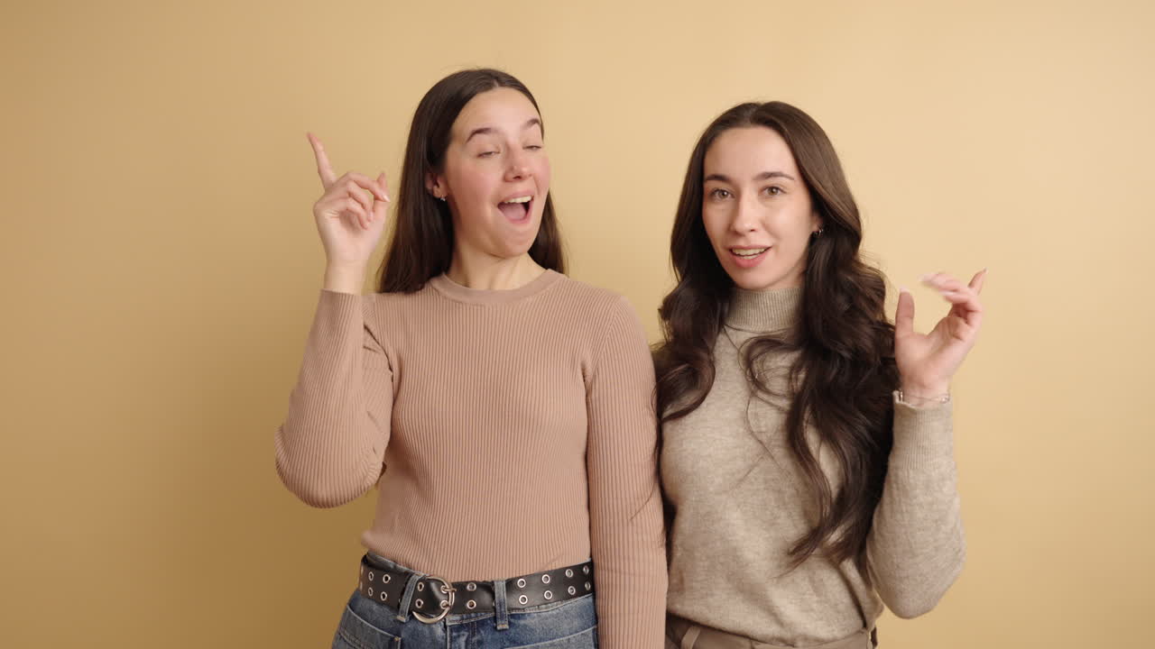 Young women pointing fingers and making faces on beige background